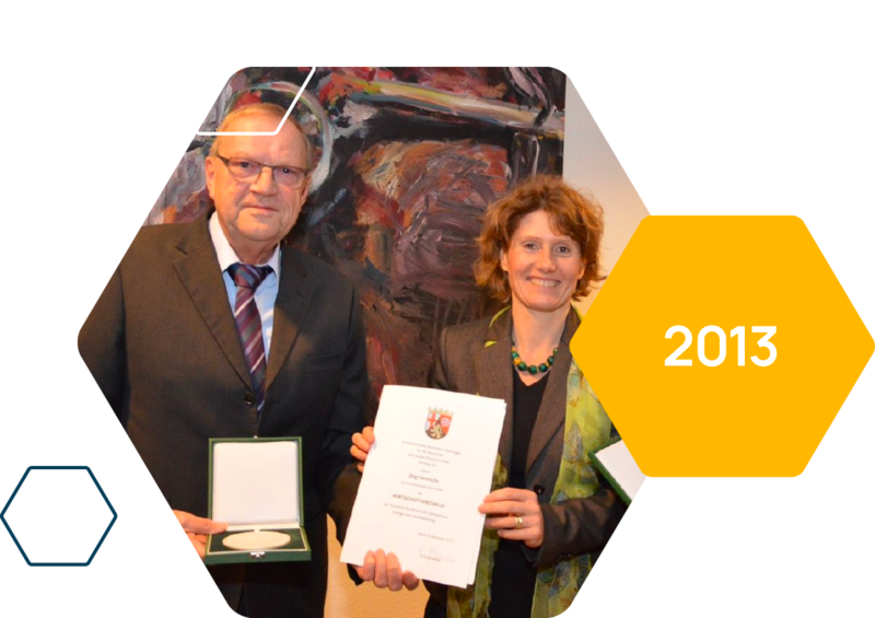 Two people hold up the medal and certificate